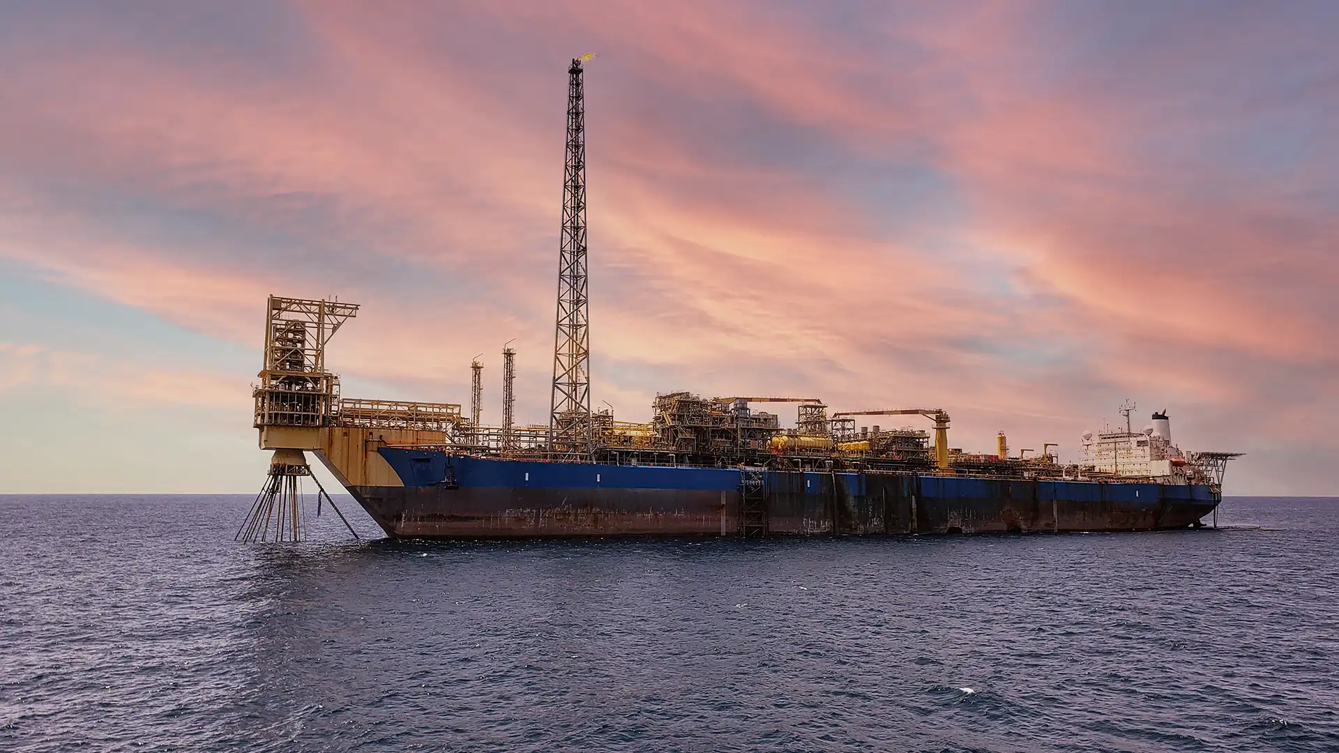FPSO vessel at sea during sunset with offshore processing equipment and flare tower visible.