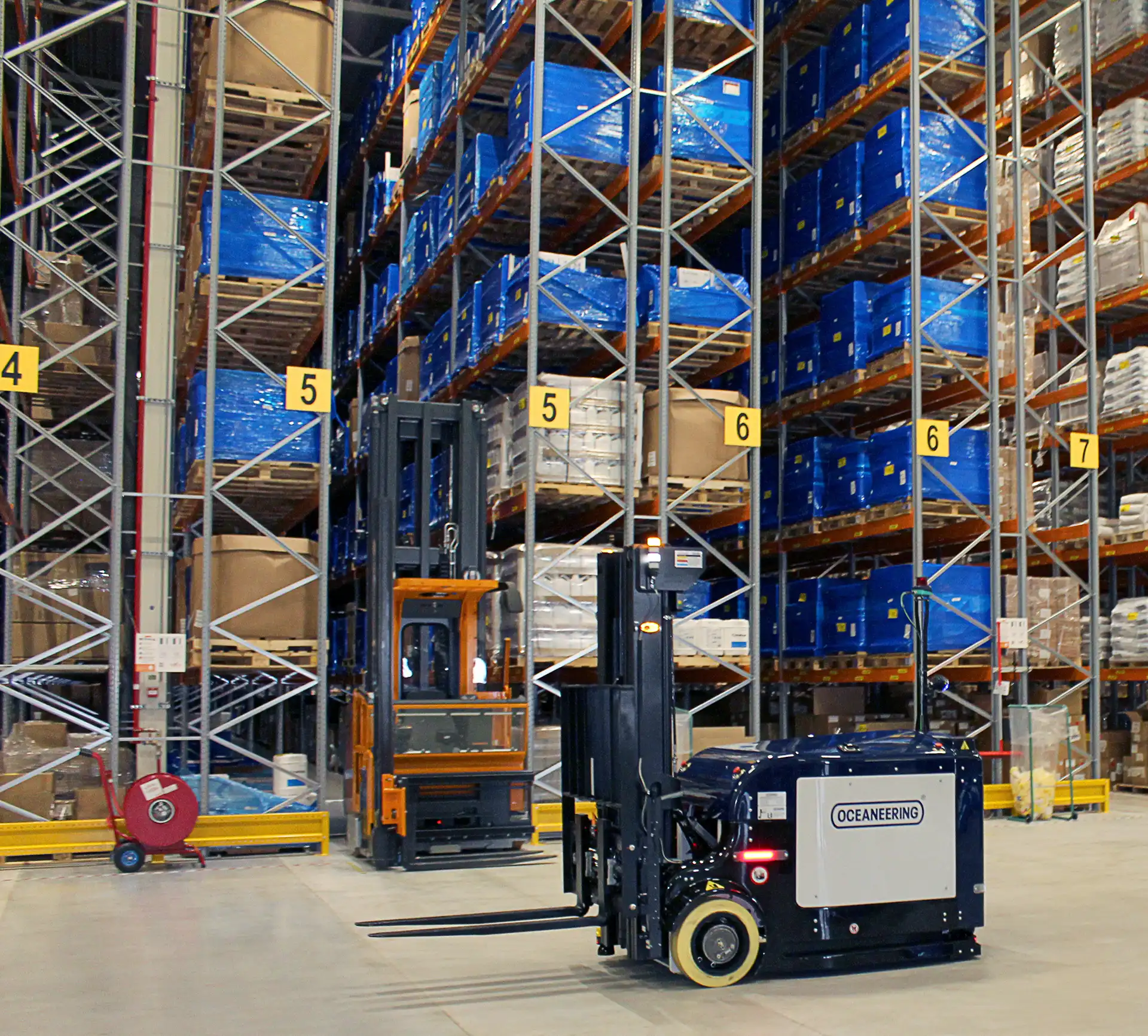 Autonomous Oceaneering MaxMover™ vehicle transporting pallets in a high bay warehouse navigating between storage racks filled with palletized inventory