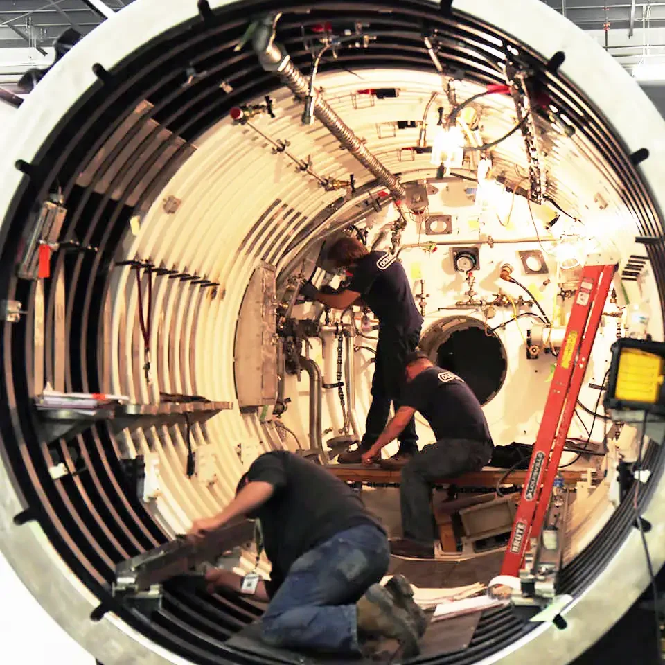 Three technicians inside a deep submergence system performing modernization tasks surrounded by tools and equipment